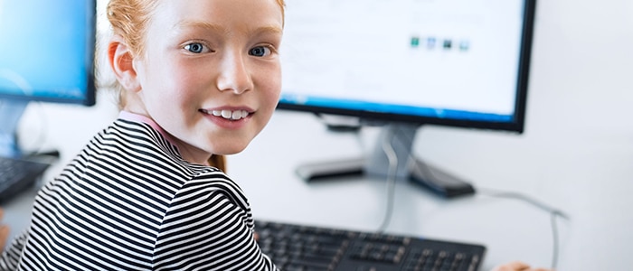 Smiling student sitting in front of a computer, turning to smile at the camera. 2024 EdTech App report.